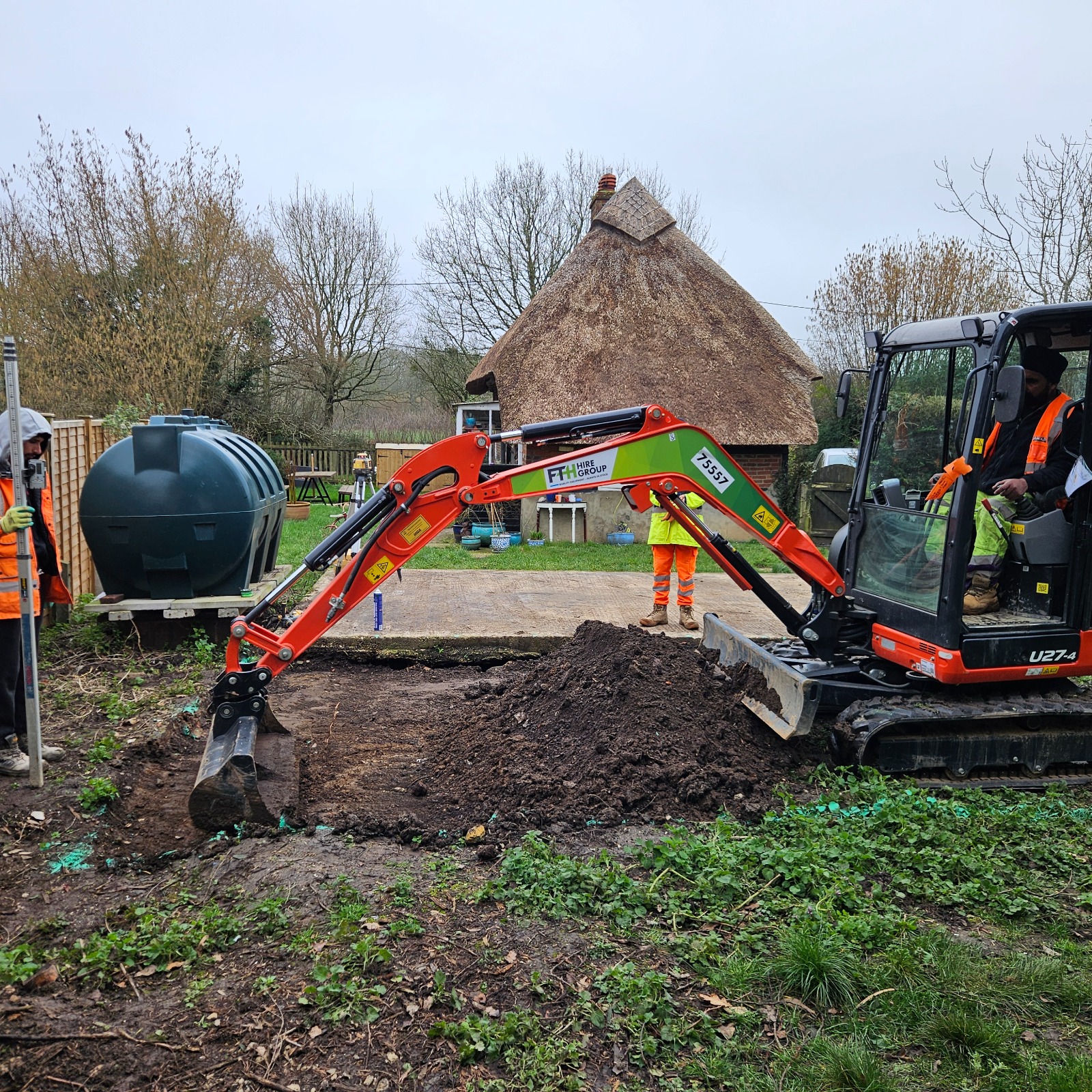 Mini digger excavating for the slab extension beside a thatched cottage in Basingstoke