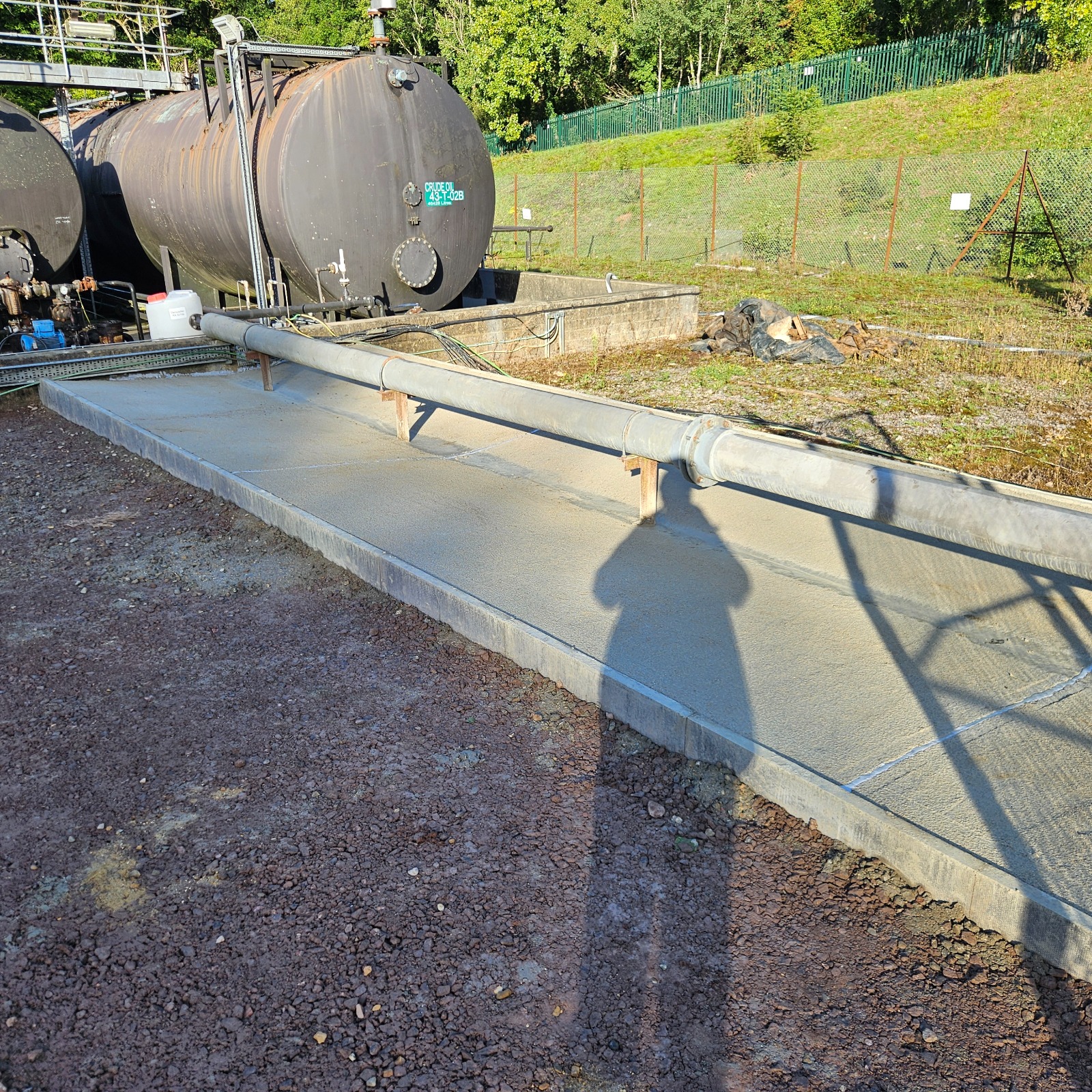 Completed concrete bund with 150 mm edging under an operational oil pipeline